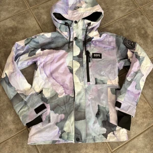  Dope skid- och snowboardjacka XS med lila camomönster - Säljer en snygg skid-och snowboardjacka från Dope i storlek XS med camomönster i lila, grått och vitt. Jackan har huva som passar hjälm och dragkedja med knappar samt kardborre framtill, samt praktiska fickor och justerbara muddar. Mellanvikts vaddering för perfekt balans mellan värme och prestanda (60g/m2 kropp, 40g/m2 ärmar och huva).  Mycket fint skick. Lite trådar inne i jackan i luvan (se bild)  som varit hela tiden sedan nyköp. Inget som syns eller påverkar funktionen. 