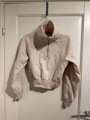 Kort tjocktröja med hög krage  - Beige tjocktröjan med muddar på ärmar och midja. Dragkedja upptill vilket är väldigt skönt när det blåser.