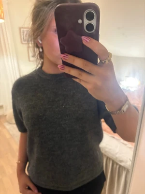 Mörkgrå stickad tröja med kort ärm - Mysig mörkgrå stickad tröja med korta ärmar och rund halsringning. Perfekt att slänga på sig när det är lite kyligare ute. Enkel och stilren design som funkar till det mesta.