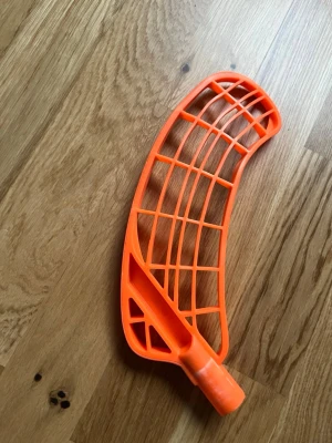 Orange innebandyblad Zonefloorball - Säljer ett orange innebandyblad från Zonefloorball med stilren, böjd form och öppet rutmönster. Bladet är tillverkat i slitstark plast och har en tydlig logga tryckt i vitt. Perfekt för dig som vill ha ett coolt och synligt blad på planen.