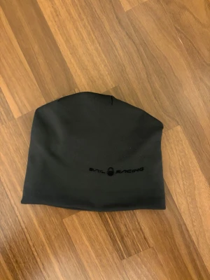  Sail Racing mössa - Svart mössa från Sail Racing med diskret logga framtill. Tillverkad i 96% återvunnen polyester och 4% polyuretan, vilket gör den både mjuk och följsam. Enkel och stilren design som passar perfekt för kalla dagar.
