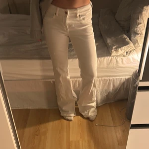 Vita bootcut jeans med hög midja - Säljer ett par vita jeans med bootcut-snitt och hög midja. Byxorna har klassiska fickor fram och bak, samt knapp och dragkedja i midjan. Materialet är jeans och passformen är loose med breda ben. Perfekt för dig som gillar en clean och stilren look.