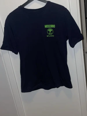 Moschino T-shirt - Moschino T-shirt som är i väldigt bra skick. Endast använd fåtal gånger. Köpt på Johnells. Original pris 2399kr.