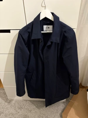 Mörkblå rock från NN07 - Snygg mörkblå rock från NN07 med klassisk krage och knäppning framtill. Jackan har en stilren och rak passform, samt praktiska fickor på sidorna. Perfekt för dig som gillar minimalistisk och clean stil.