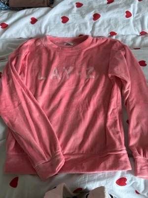 Rosa fleece-tröja LAY-Z - Mjuk och gosig rosa fleece-tröja från C med trycket 'LAY-Z' på bröstet. Tröjan har rund hals och långa ärmar, perfekt för chilliga dagar. Passar dig som gillar bekväma och snygga plagg med lite attityd.