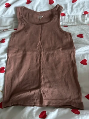 Brun linnetopp från 157, storlek 160 - Säljer en enkel och stilren brun linnetopp från 157 i storlek 160. Toppen är ärmlös med rund halsringning och tillverkad i mjuk bomull. Perfekt att matcha med jeans eller shorts för en chill look.