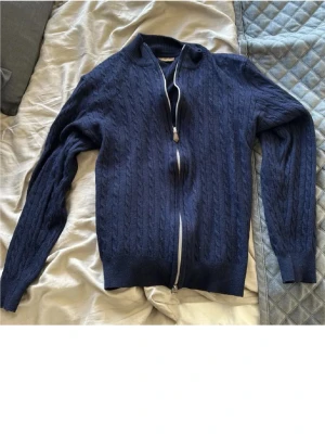 Mörkblå stickad kofta från Stenströms - Säljer en mörkblå stickad kofta från Stenströms med snyggt kabelmönster. Koftan har långärmade ärmar, ribbad krage och muddar samt en silverfärgad dragkedja framtill. Perfekt för dig som gillar klassisk stil med en modern twist. Den passar en som är runt 165-170 cm lång. Det är bara att höra av sig vid frågor och funderingar 😀