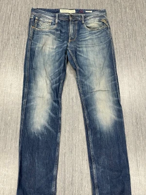 Replay Anbass jeans blå straight fit - Vi kan gå ner i pris vid snabb affär!                Snygga Replay Anbass jeans i blå tvätt med slitningar och kontrastsömmar. Klassisk femficksmodell med raka ben och normal passform. Jeansen har låg midja och är tillverkade i slitstarkt bomullsjeansmaterial. Perfekt för dig som gillar en cool och avslappnad stil. 