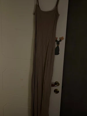 Beige långklänning med smala axelband - Säljer en enkel och stilren beige långklänning med smala axelband. Klänningen har en rak och loose passform som faller snyggt längs kroppen. Perfekt för dig som gillar minimalistisk stil och vill ha något bekvämt och luftigt.