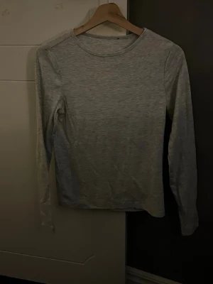Ljusgrå långärmad topp - En enkel och stilren ljusgrå långärmad topp i mjukt material. Perfekt basplagg med rund halsringning och normal passform. Passar till allt och är superenkel att matcha med olika outfits.