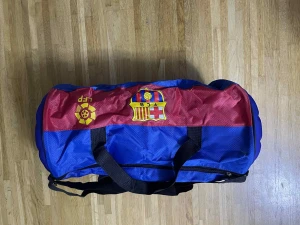 FC Barcelona träningsväska blå/röd - Säljer en sportig träningsväska från FC Barcelona i blått och rött med klubbens emblem på sidan och botten. Väskan har svarta handtag och axelrem, samt ett coolt fotbollsmönster på botten. Perfekt för gymmet eller fotbollsträningen!
