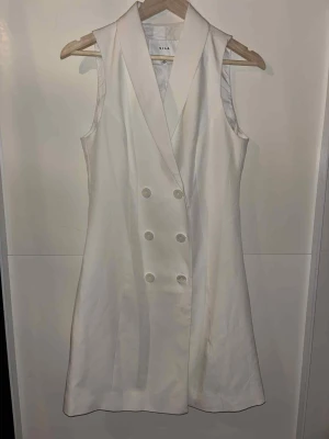 Vit ärmlös byxdress från Vila - Snygg vit ärmlös byxdress från Vila med dubbelknäppning framtill och breda slag. Stilren design som ger en chic look, perfekt för dig som gillar att sticka ut. Materialet känns mjukt och har en lätt glans. Passar dig som vill ha något annorlunda och trendigt. Inte använd någon gång