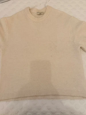 Beige stickad tröja från gina  - Säljer en stilren beige stickad tröja från Rodebjer. Tröjan har rund halsringning, ribbade muddar och en klassisk, normal passform. Perfekt för lager-på-lager under kyliga dagar. Superenkel att matcha med jeans eller kjol.