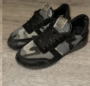 Valentino rockrunners - Säljer ett par snygga Valentino Garavani sneakers med svart och grått camouflagemönster. Skorna har snörning, rund tå och platt sula. Ovandelen är i mesh och mocka, vilket ger en cool och sportig vibe. Perfekta för dig som gillar streetstyle och exklusiva märken. Pris ej hugget i sten 🪨 
