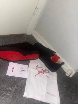Christian Louboutin svarta sneakers med nitar - Svarta sneakers från Christian Louboutin med röd signatursula och svarta nitar på tån. Skorna är gjorda i mocka och har snörning. Innersulan har röd detalj med logga. Medföljer dustbag och äkthetskort.