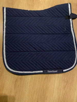 Marinblått dressyr schabrak från HorseGuard - Snyggt marinblått schabrak från HorseGuard med silvrig kantdetalj. schabraket har ett stilrent mönster med snedställda ränder och är tillverkad i polyester. 