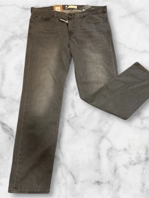 Dressmann grå jeans 38/32 – Lightweight Rigid – Nya med prislapp - Snygga grå jeans från Dressmann i modellen Lightweight Rigid Grey. Jeansen har en klassisk 5-ficksdesign och rak passform, vilket gör dem enkla att matcha till både vardag och mer uppklädda tillfällen.  Tillverkade i ett lättare, stadigt denimtyg utan stretch för en mer klassisk känsla. Färgen är grå med lätt tvätt för ett stilrent och modernt uttryck. 	•	Märke: Dressmann 	•	Storlek: 38/32 	•	Färg: Grå 	•	Modell: Lightweight Rigid 	•	Passform: Rak / klassisk 	•	Skick: Ny med prislapp Nypris:299 