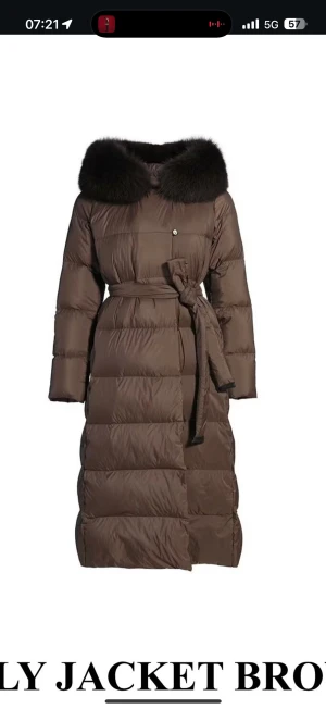 Brun lång dunjacka med päls - Snygg brun dunjacka med fluffig mörk päls runt kragen och ett bälte i midjan för extra stilpoäng. Jackan är lång, har quiltad design och långa ärmar. Perfekt för kalla dagar när du vill vara både varm och trendig. Precis köpt så knappt använd och säljs pågrund av icke behov