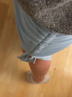 Ljusblå ribbade Tjol  med snörning - Säljer ett par ljusblå ribbade Tjol  med snygg snörning och slits på sidan. Byxorna har en loose passform och är tillverkade i ett mjukt material som känns skönt mot huden. Perfekta för chill dagar hemma eller när du vill vara bekväm men ändå se fräsch ut.