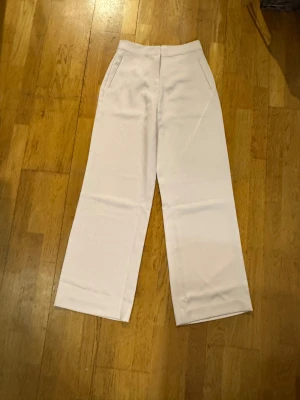 Beige wide byxor från boa, storlek S - Snygga beige byxor från boa i storlek S. Modellen är wide med hög midja och raka ben, vilket ger en chill och trendig siluett. Byxorna har sidfickor och är gjorda i ett mjukt bomullsmaterial som känns skönt mot huden.