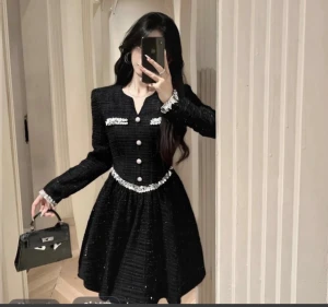 Svart kortklänning med paljettdetaljer - Supersnygg svart kortklänning med glittrig textur och paljettdetaljer i silver vid midja, bröst och ärmslut. Klänningen har lång ärm, markerad midja och dekorativa knappar framtill. Materialet är grovstickat med inslag av glansiga trådar och paljetter för extra lyxig känsla.