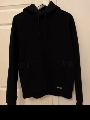 Hugo Hoodie - Fräsch svart Hugo Hoodie som går med allt, unik design med snygg luva. Rekommenderas