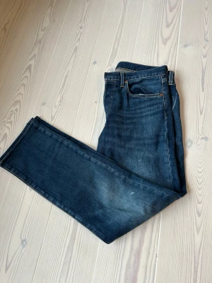 Levi's 501 - Säljer ett par klassiska Levi's 501 jeans i mörkblå tvätt. Modellen har rak passform, fem fickor och knappgylf. Premiumkvalitet med snygga kontrastsömmar och ikonisk läderpatch bak i midjan. Perfekt för dig som gillar tidlös denimstil. ♦️Jeansen har några små färgfläckar som går att tvätta bort ♦️
