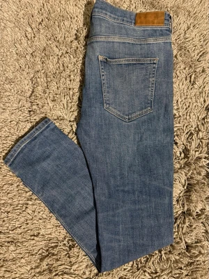 Blå skinny jeans från GANT - Säljer ett par snygga blå jeans från GANT med klassisk fyraficksdesign och brunt läderpatch bak i midjan. Jeansen har skinny passform och är tillverkade i mjukt denimtyg med lätt tvättad look. Perfekta för dig som gillar stilrena och smala jeans.