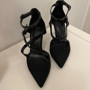 Svarta pumps med remmar från Bershka - Snygga svarta pumps från Bershka med spetsig tå och flera smala remmar som korsar foten och går runt ankeln. Skorna har låg klack och är gjorda i mocka och skinnimitation. 