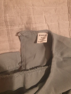 grön långklänning med volang från SHEIN - Superfin grön långklänning från SHEIN Teen med bred volang upptill och långa ärmar med rynkade muddar. Klänningen har ett brett bälte med en snygg guldfärgad ringdetalj i midjan. Materialet är lätt och känns som polyester.