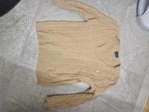 Beige kabelstickad tröja Polo Ralph Lauren - Snygg beige kabelstickad tröja från Polo Ralph Lauren med v-ringad hals och långa ärmar. Tröjan har klassisk kabelmönster och är tillverkad i mjuk bomull, perfekt för dig som gillar stilrena och tidlösa plagg. Bleknat lite av tvätt men syns knappt. Inga andra defekter.