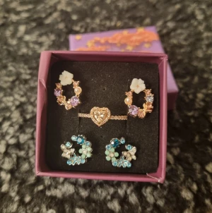 Set med örhängen och ring Strl 8(57) - Supergulligt smyckeset med två par örhängen och en ring. Ringen är roséguldfärgad med ett rosa hjärta av glittrande stenar. Material : koppar 