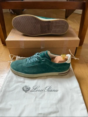 Gröna mockasneakers från Loro Piana - Snygga gröna sneakers från Loro Piana i mjuk mocka med vit detalj vid hälen och platt sula. Skorna har rund tå och klassisk snörning. Perfekta för dig som gillar exklusiva och stilrena sneakers med premiumkänsla. MÖTS BARA ‼️