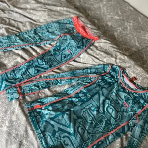 Mönstrat Underställ Kari Traa - Säljer ett underställ från Kari Traa i storlek S. Tröjan har ett coolt geometriskt mönster i blått och turkost med kontrasterande korallröda sömmar. Materialet är mjukt och stretchigt polyester, perfekt för träning eller som underställ.