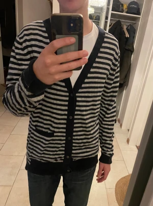 Kaschmir kofta från Acne i svart grå - Säljer en snygg archive randig kofta från Acne i svart och grått. Acne studios. Koftan har v-ringning, knappar hela vägen och en liten ficka framtill. Perfekt att slänga över en t-shirt för en chill look. Är cachmire bladning och väldigt mysigt material