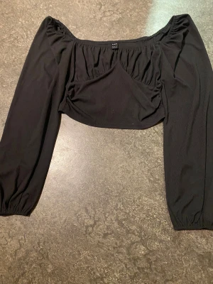 Svart croppad bolerotopp från SHEIN - Säljer en svart croppad bolerotopp från SHEIN i storlek S. Toppen har offshoulder-design med långa ärmar och är gjord i ett ribbat syntetmaterial. Perfekt för att styla med höga jeans eller kjol för en trendig look.