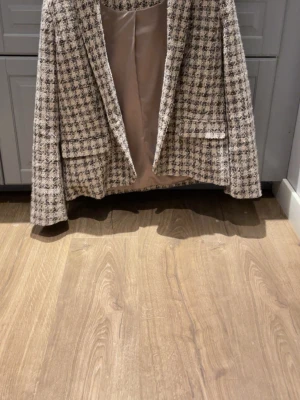 Rutig beige kavaj från CRO - Säljer en snygg rutig kavaj från CRO i beige och svart. Kavajen har klassisk krage, två fickor fram och är helfodrad med glansigt tyg. Materialet är grovt vävt och ger en cool, lite retro känsla. Perfekt för dig som vill sticka ut med stil.