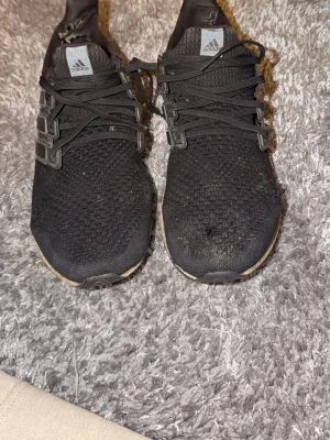 Svarta Adidas Ultraboost sneakers stl 46 - Säljer ett par svarta Adidas Ultraboost sneakers i storlek 46. Skorna har stickad ovandel, svarta snören och en beige boost-sula. Klassisk Adidas-logga på plösen och de ikoniska tre ränderna på sidan. Perfekta för dig som gillar sportig stil.