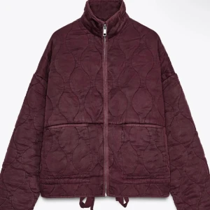 Quiltad vinröd jacka från Zara - Quiltad jacka från Zara i vinröd färg med loose passform och höga krage. Jackan har dragkedja framtill, två stora fickor och snörning nedtill. Materialet är mjukt och känns som bomull, perfekt för höst och vinter. Snygg och chill stil som passar till jeans eller tights.