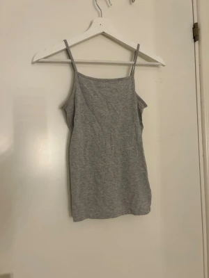 Grå linnetopp med smala axelband - Säljer en enkel och stilren grå linnetopp med smala axelband. Toppen har en rak och slim passform och är tillverkad i mjuk bomullsmix som känns skön mot huden. Perfekt att matcha med jeans eller shorts under varma dagar.