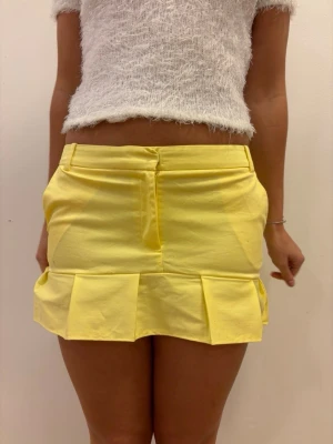 Gul kortkjol med volangkant😍 - Superfin gul kortkjol med bred volangkant längst ner. Kjolen har fickor på sidorna, bälteshällor och en dold dragkedja fram. Perfekt för dig som vill vara extra fin till sommaren!🌴💕 Denna är egensydd av oss från ett par gula kostymbyxor!