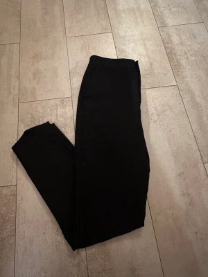 Svarta kostymbyxor från Gina Tricot - Stilrena svarta kostymbyxor från Gina Tricot i storlek S. Byxorna har rak passform, klassisk midja och stängs med knapp och dragkedja. Materialet är mjukt och känns skönt mot huden. Perfekta för dig som gillar en clean och enkel look.