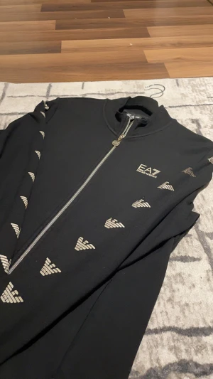 Svart zip hoodie EA7 Emporio Armani - Svart kofta från EA7. Koftan är som ny och passar både Killar och tjejer, den är i jätte bra skick och är knappt använd. Inga skador eller liknande, Håller dig stilig och skön.