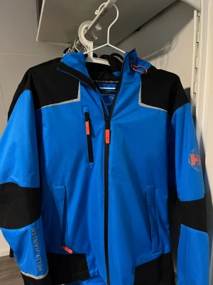 Blå och svart vindjacka Helly Hansen - Säljer en blå och svart vindjacka från Helly Hansen Workwear med huva. Använd fåtal gånger, i princip nyskick. Jackan är i storlek S. Nypris: ~1500