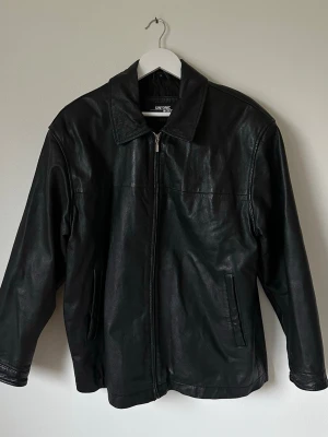 Svart skinnjacka från GinTonic - Svart skinnjacka från GinTonic i klassisk modell med krage och dragkedja framtill. Jackan har två sidofickor och är helsvart både på utsidan och insidan. Perfekt för dig som gillar en stilren och tidlös look. 7Y3