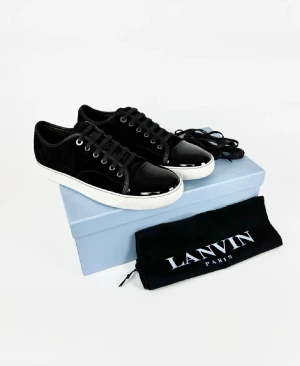 Svarta sneakers från Lanvin med lackad tå - Snygga svarta sneakers från Lanvin med vit platt sula och lackad tå. Skorna har snörning och en stilren design med silverfärgade öljetter. Ovandelen är i mocka och tåpartiet i blankt skinn, vilket ger en cool kontrast. Perfekt för dig som gillar exklusiva detaljer.