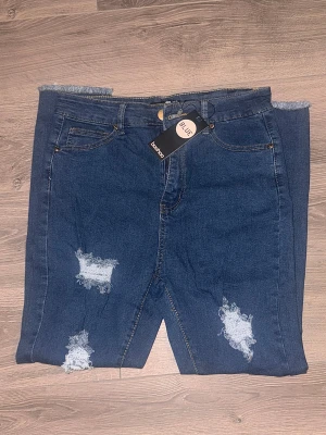 Blå ripped jeans från Boohoo Blue - Snygga blå jeans från Boohoo Blue med slitna detaljer och fransade benslut. Modellen har klassisk femficksdesign, knapp och dragkedja framtill. 
