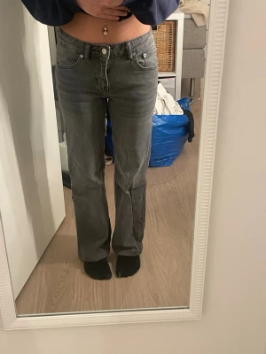 Grå bootcut jeans med fickdetaljer - Säljer ett par grå jeans med bootcut-snitt och klassiska fem fickor, inklusive bakfickor med lock och knapp från lager 157. Jeansen har hög midja och är tillverkade i ett slitstarkt denim-material. Perfekt för dig som gillar en avslappnad men snygg stil.