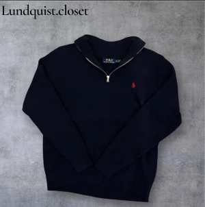 Marinblå quarter zip från Polo Ralph Lauren - Snygg marinblå stickad tröja från Polo Ralph Lauren med röd logga på bröstet. Tröjan har lång ärm, ribbade muddar och en half zip-dragkedja vid halsen. Storlek M men passar också väldigt bra som storlek S