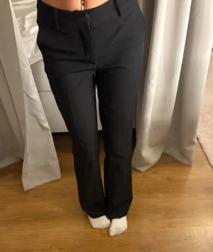 Svarta kostymbyxor med bootcut - Snygga svarta kostymbyxor med klassisk bootcut-passform. Byxorna har pressveck, hällor för bälte och stängs med dragkedja och knapp. Perfekta för en clean och stilren look. Materialet känns mjukt och följsamt.